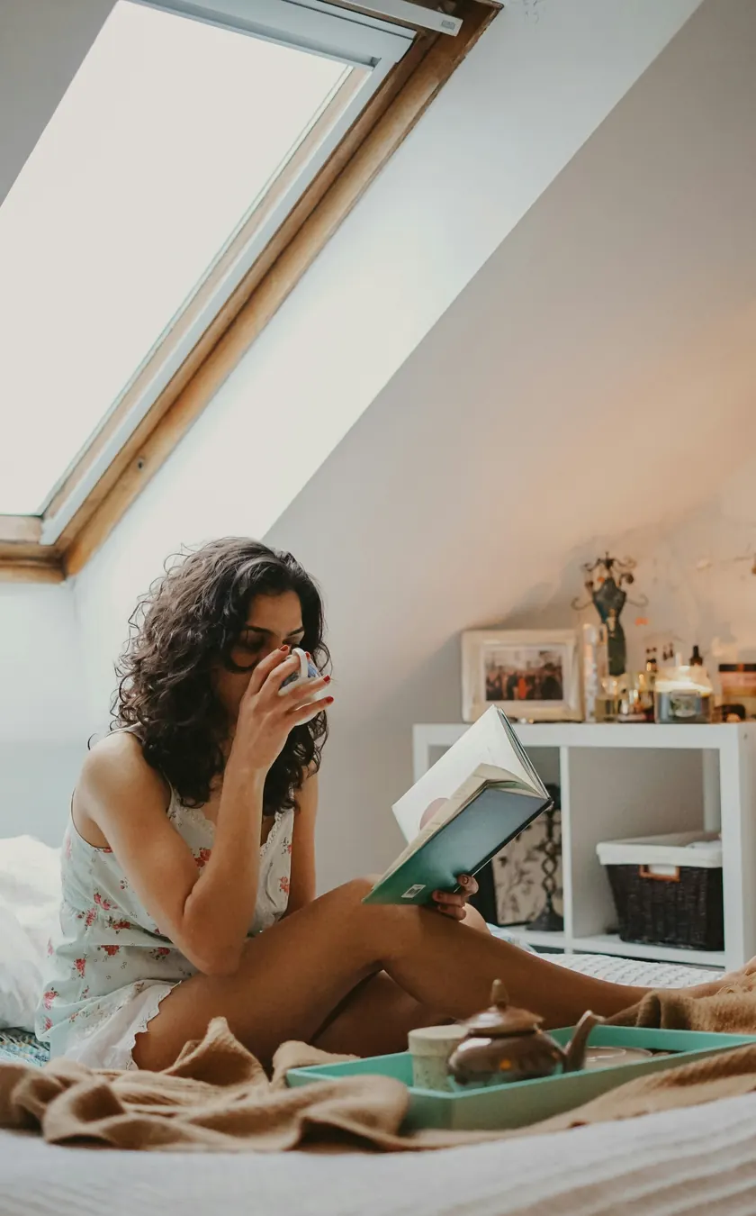 Woman reading a book with a cup of tea in bed